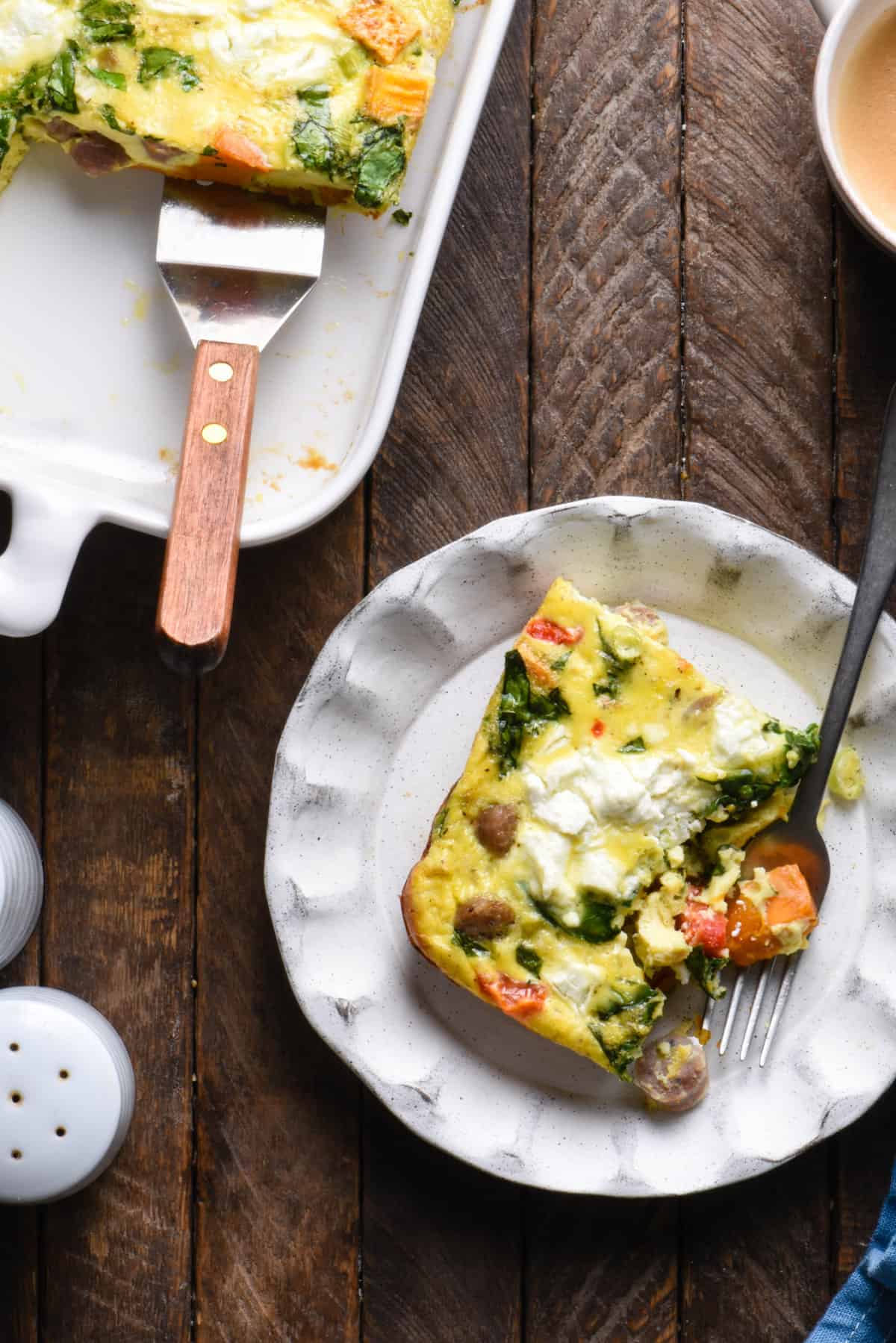 One piece of sweet potato egg bake on small plate with fork, on a wooden surface.