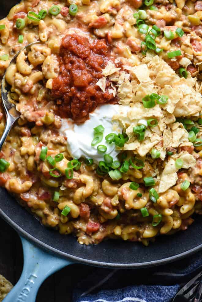 Closeup on elbow macaroni and cheese with ground beef, topped with salsa and sour cream.