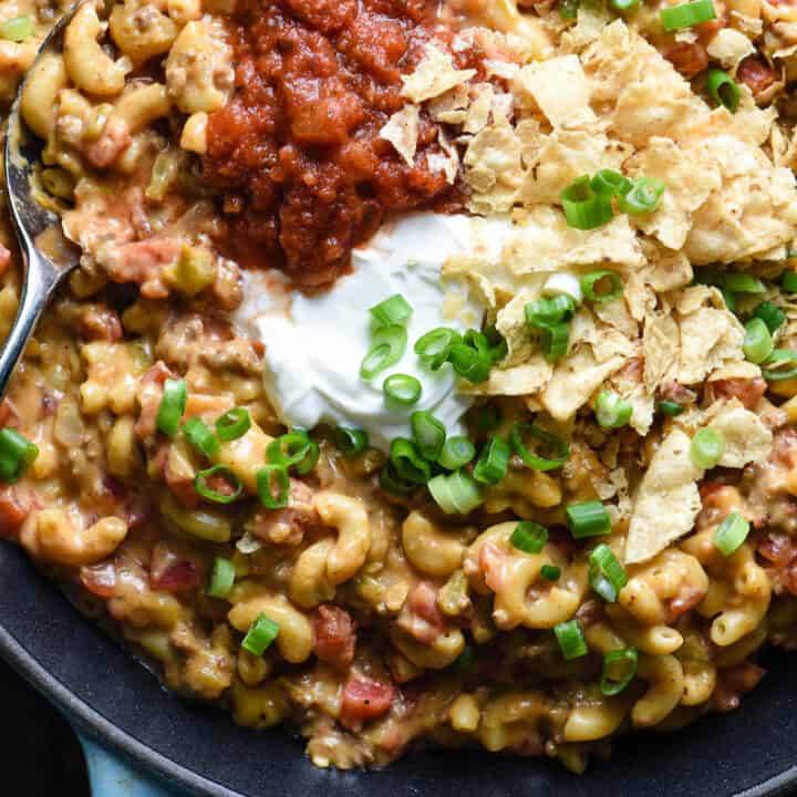 Skillet filled with taco mac and cheese, toped with salsa, sour cream crushed tortilla chips and green onions.