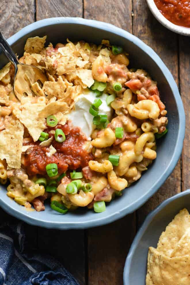 Small blue bowl of mac and cheese with ground beef, topped with sour cream and salsa.