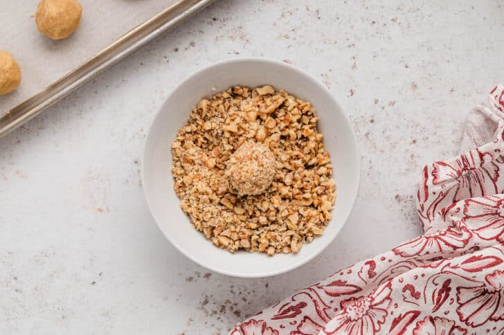 A small ball of light brown dough in a small white bowl filled with chopped walnuts.