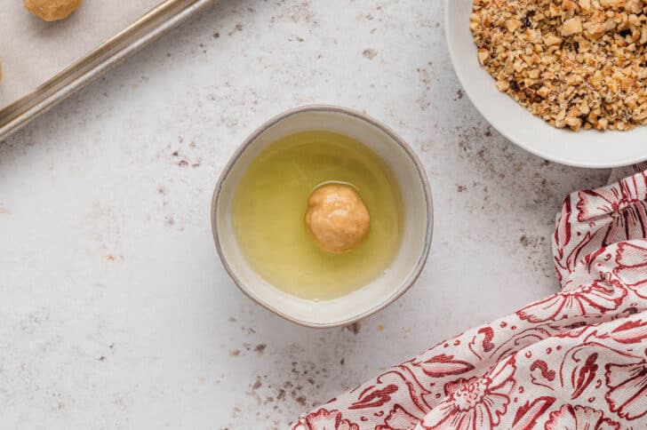 A small ball of light brown dough in a small white bowl filled with egg whites.