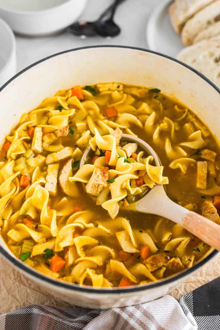 A white Dutch Oven with a ladle scooping out some turkey soup recipe.