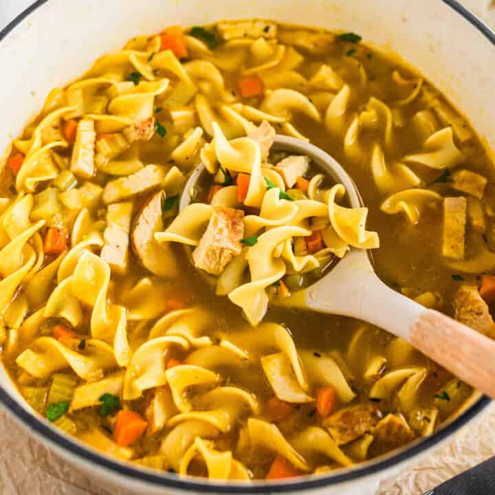 A white Dutch Oven with a ladle scooping out some turkey soup recipe.