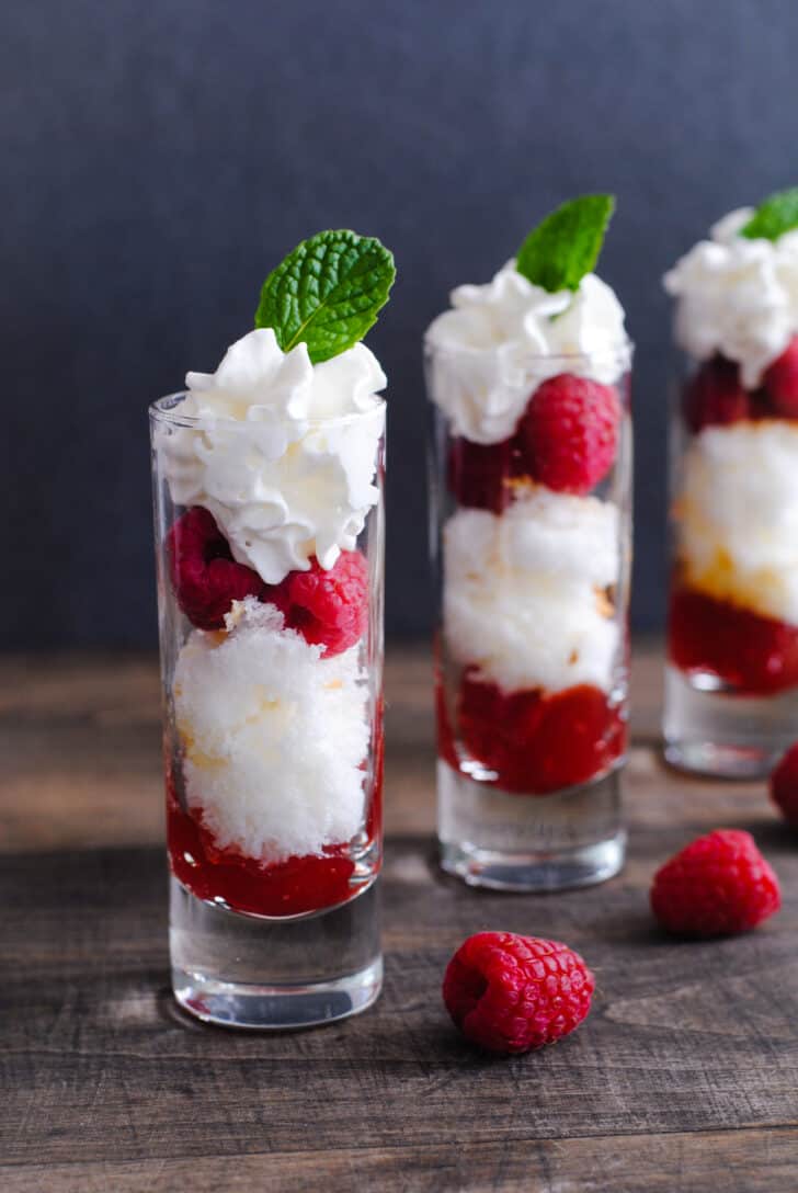 A Valentine's dessert made in three tall shot glasses, with layers of cake, raspberries, red jam and whipped cream.