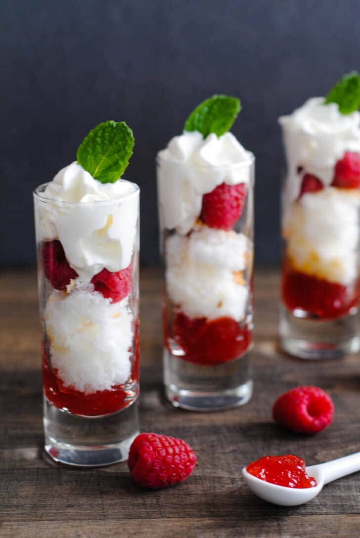 A Valentine's dessert made in three tall shot glasses, with layers of cake, raspberries, red jam and whipped cream.