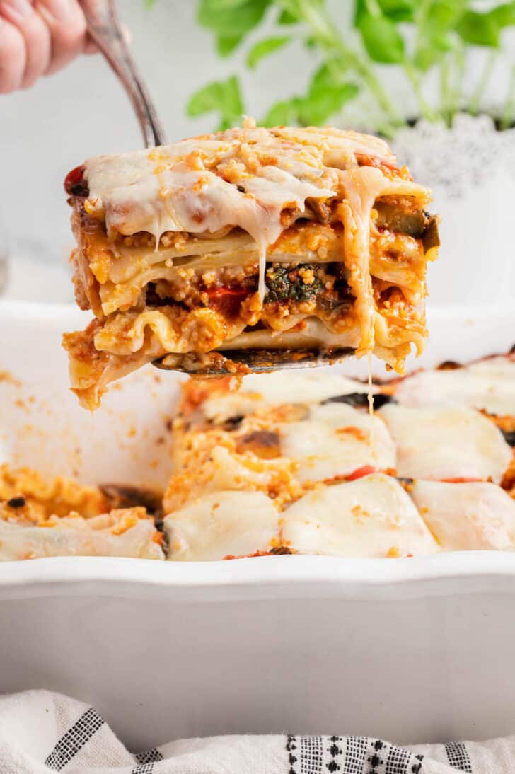A piece of vegetable lasagna being lifted out of a white baking dish.