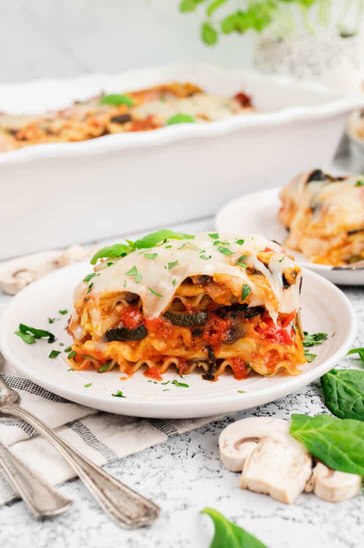 A slice of veggie lasagna garnished with green herbs on a small white plate.