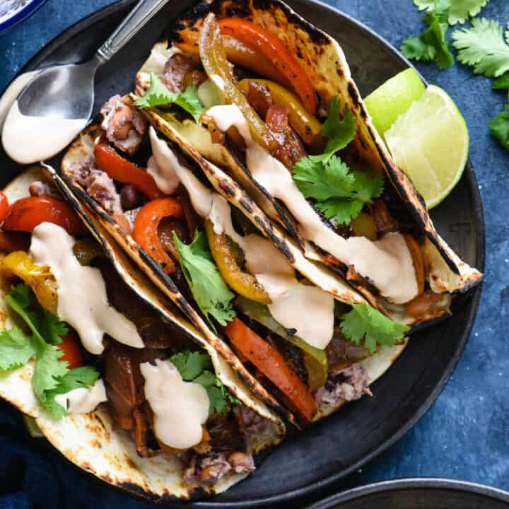 Overhead photo of three vegetarian fajitas on black plate with lime wedges.