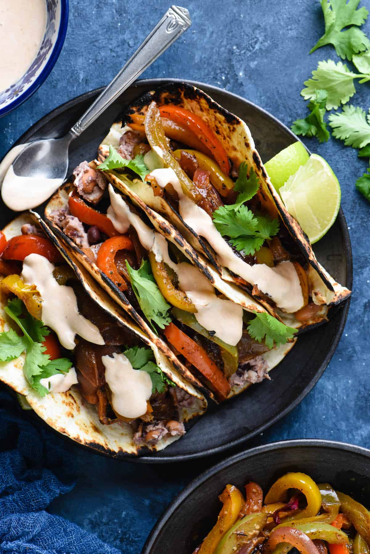 Overhead photo of vegetable fajitas on black plate and blue background.