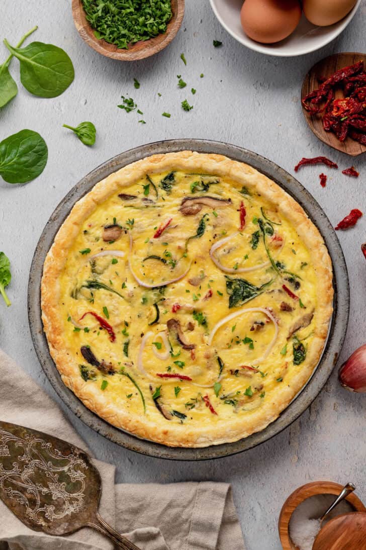 A metal pie tin filled with a savory egg pie filled with vegetables.