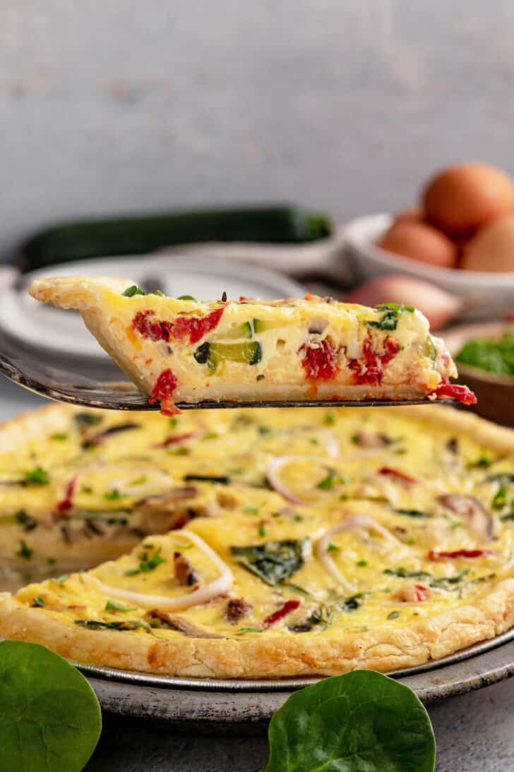 A slice of vegetable quiche being lifted out of a full quiche in a metal pie plate.